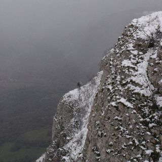 Une falaise partiellement enneigée sous un ciel gris, photographiée depuis le sommet